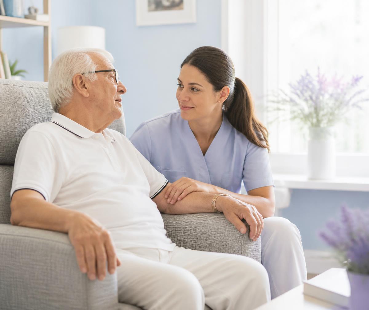 Caregiver sitting beside an elderly man, listening attentively during a conversation